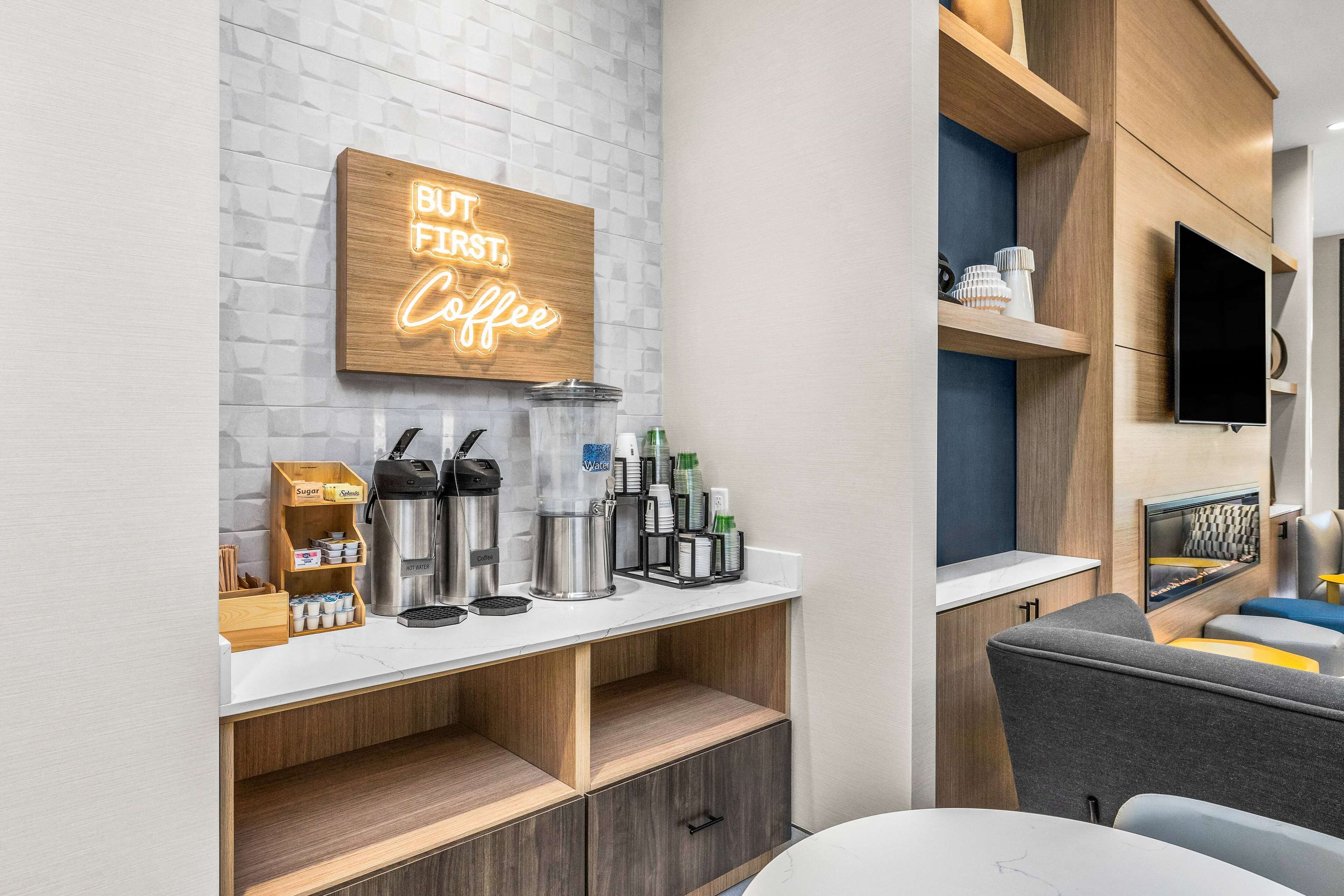 Estação de café moderna com letreiro neon, máquinas de café e uma TV na parede.
