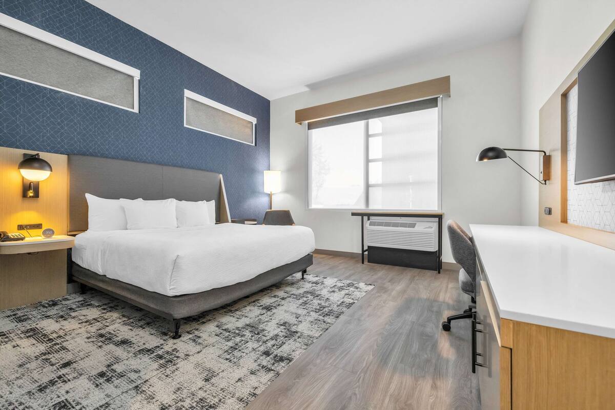 Une chambre d’hôtel moderne, dotée d’un grand lit, d’un bureau et d’une fenêtre avec stores.