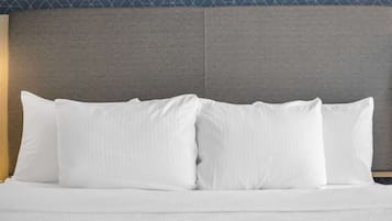 Una cama con ropa de cama y almohadas blancas, cabecera gris y un papel tapiz estampado al fondo.