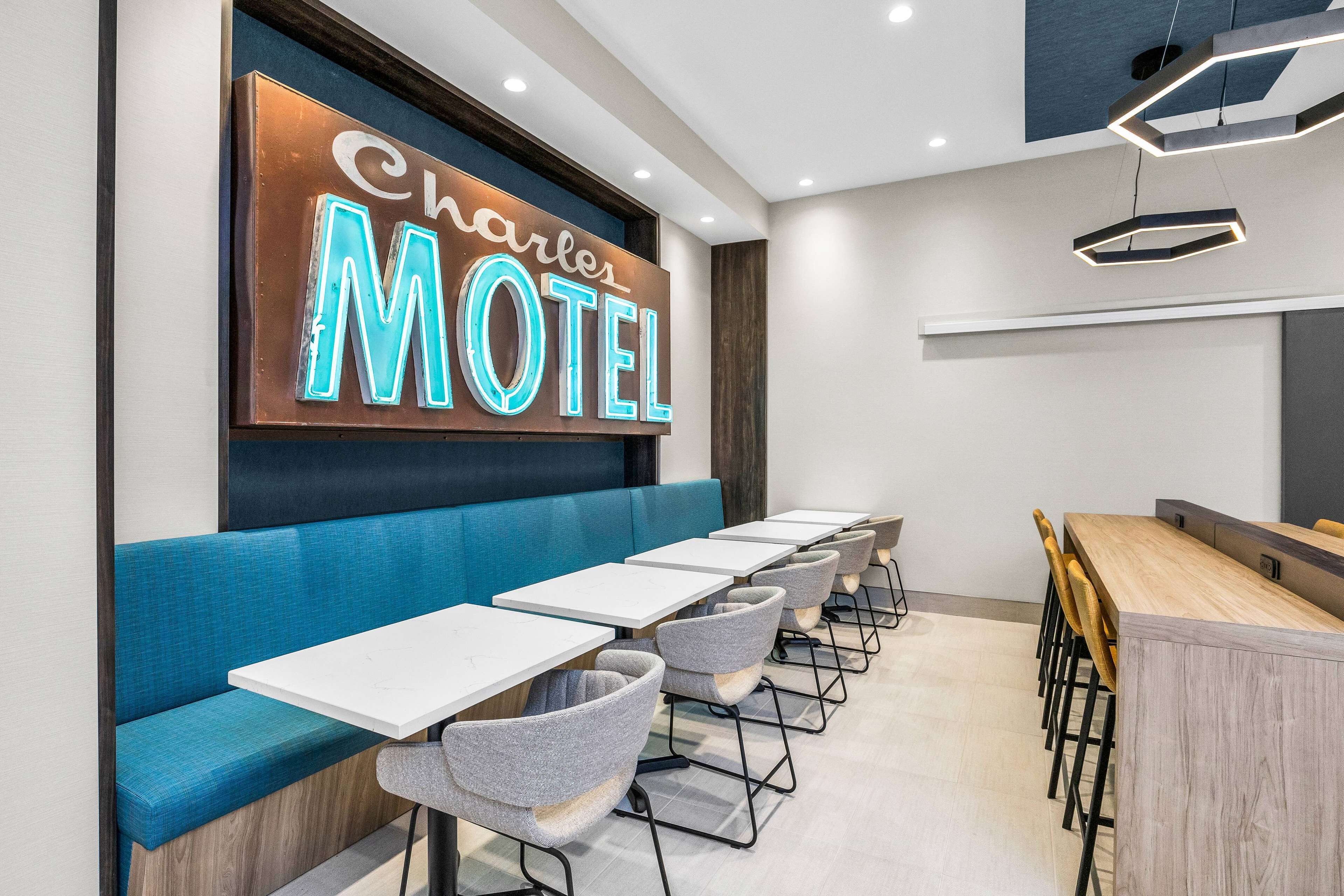A motel interior with a neon sign, blue seating, and a long dining table.