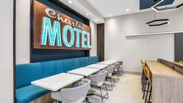 A motel interior with a neon sign, blue seating, and a long dining table.