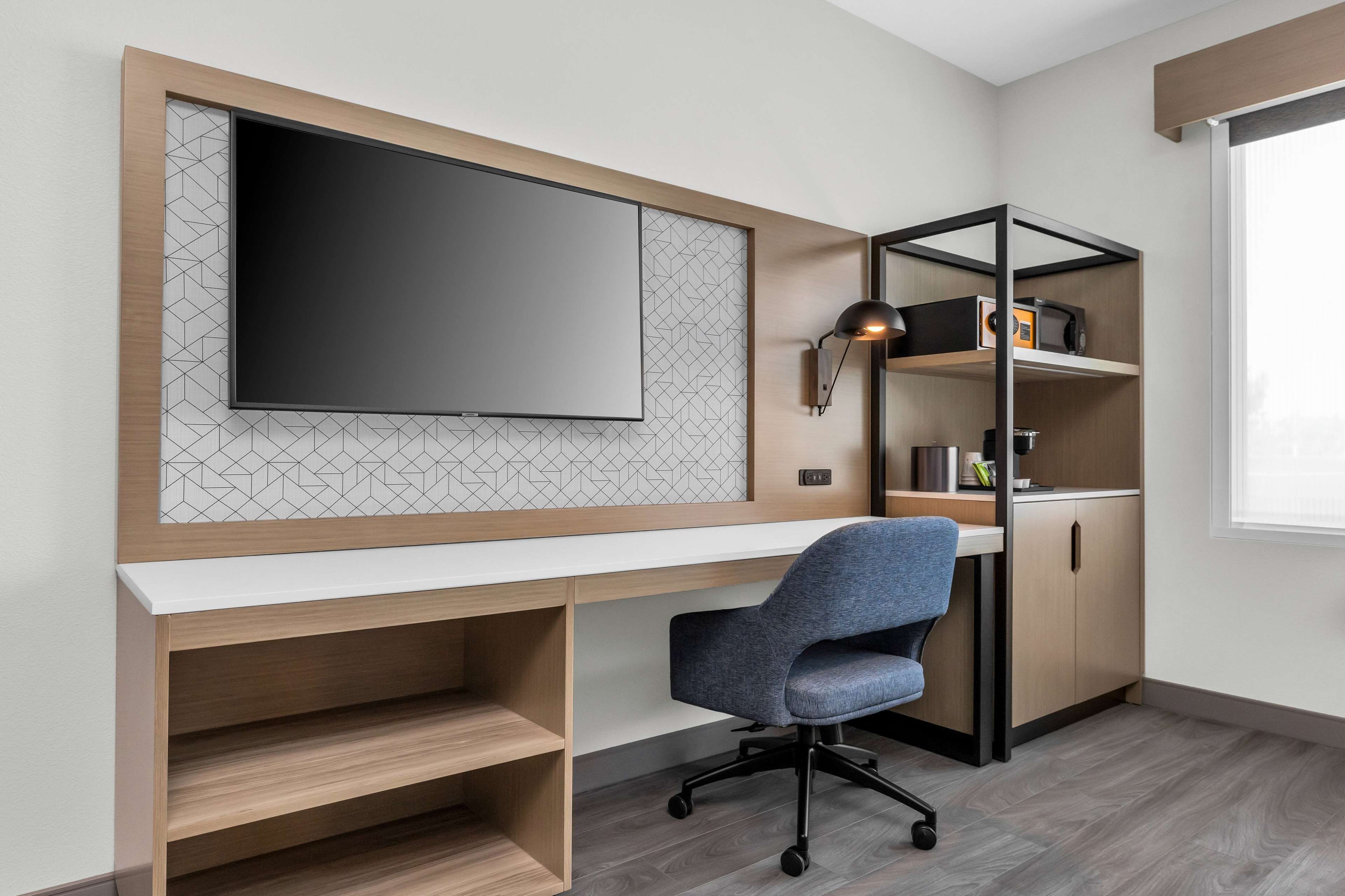 Un espacio de oficina moderno con una televisión de pantalla plana grande, un escritorio, una silla de oficina azul y estanterías empotradas con una radio y utensilios de cocina.