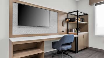 Un espacio de oficina moderno con una televisión de pantalla plana grande, un escritorio, una silla de oficina azul y estanterías empotradas con una radio y utensilios de cocina.
