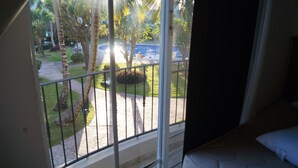 Ein Balkon mit Blick auf einen Swimmingpool, Palmen und einen gepflegten Rasen.