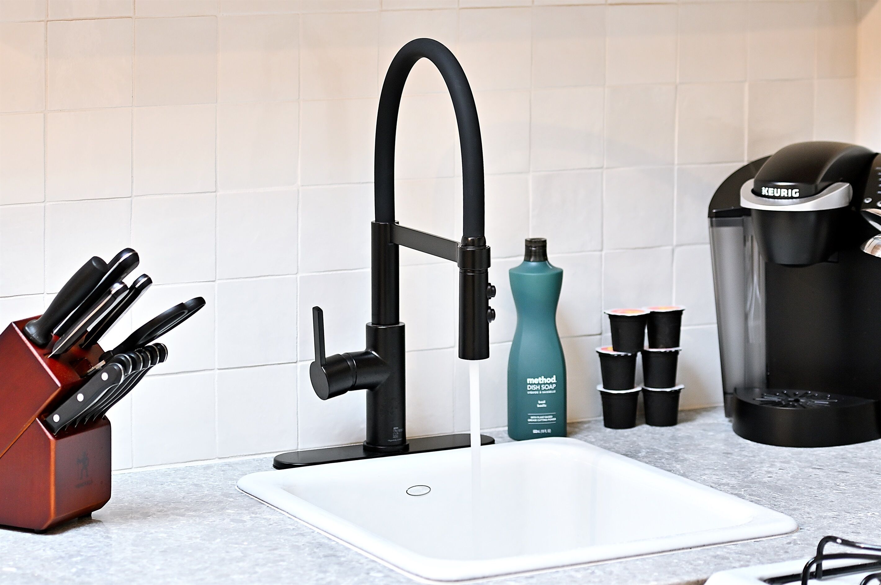 A kitchen with a modern faucet, a coffee maker, a knife block, and dish soap.