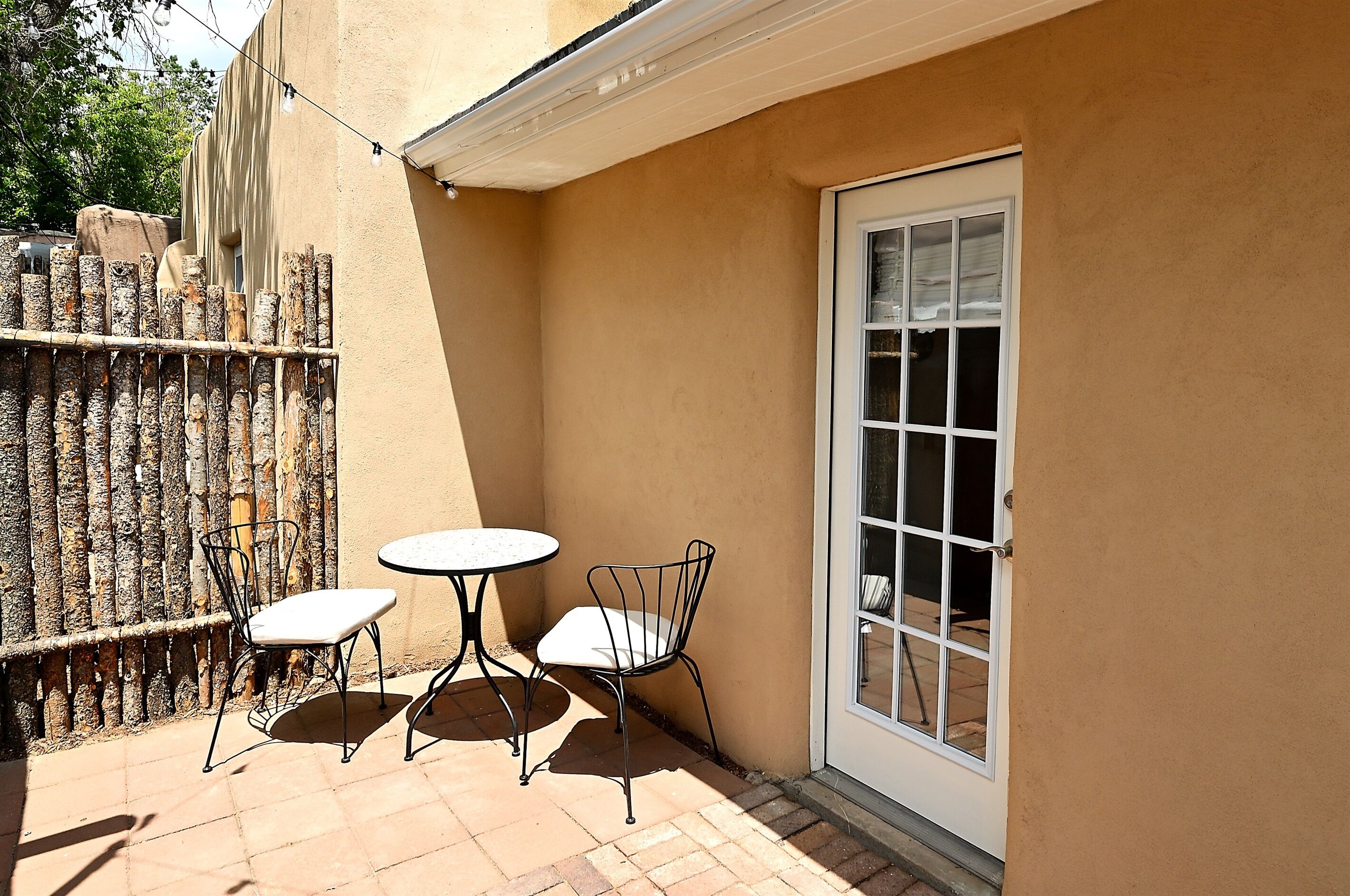A patio with two metal tables and chairs, a wooden fence, and a sliding glass door.