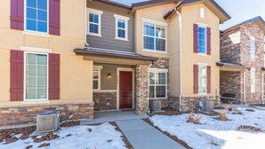 A two-story house with a stone facade, a front porch, and a snow-covered driveway. - Luxury Brand New Townhouse, family and pet friendly (Highlands Ranch)