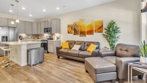 A modern kitchen with grey cabinets, a stainless steel refrigerator, and a central island. There is a grey leather sofa with yellow cushions and a potted plant. - Luxury Brand New Townhouse, family and pet friendly (Highlands Ranch)