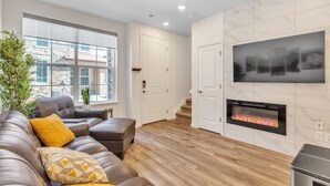 A modern living room with a leather sofa, a fireplace, and a large window overlooking a stone building. - Luxury Brand New Townhouse, family and pet friendly (Highlands Ranch)
