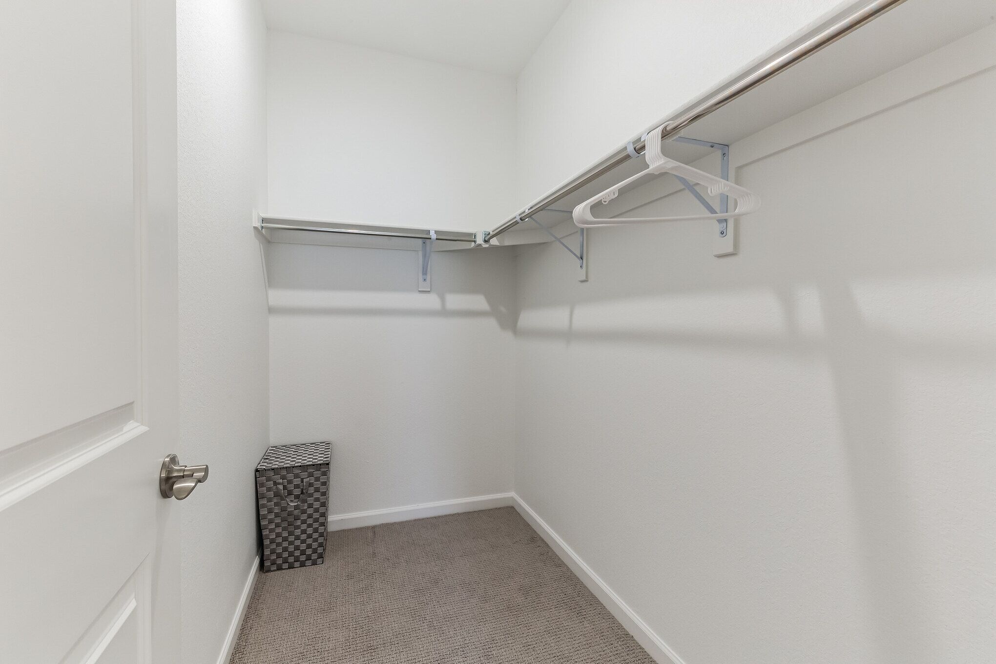 A small, white closet with a metal rod for hanging clothes, a gray storage box, and a white door.