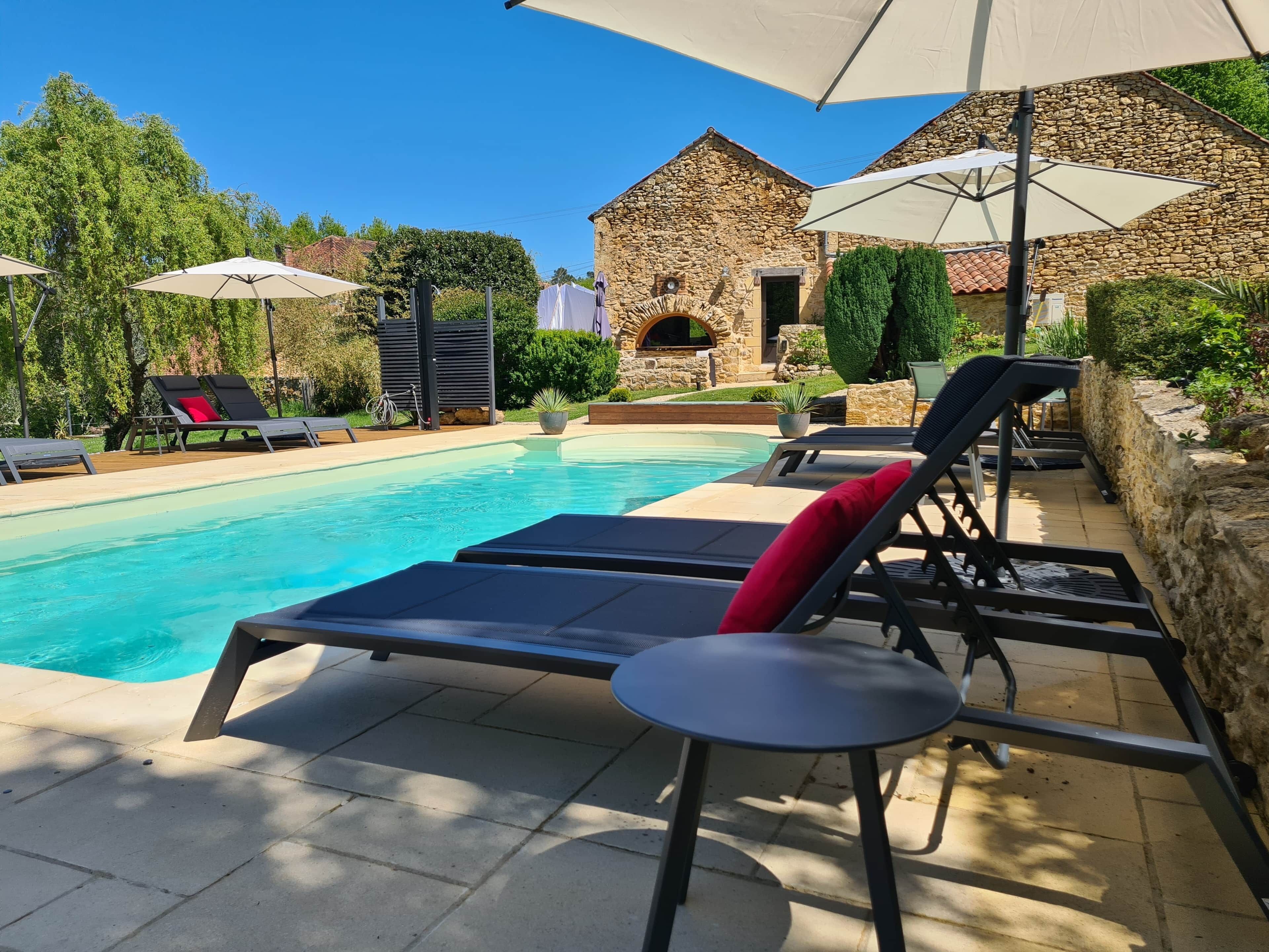 Una piscina con lettini e ombrelloni, circondata da mura in pietra e vegetazione.