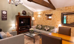 Un salon chaleureux avec un mur en pierre, un téléviseur à écran plat, un canapé, une table basse et une table à manger.