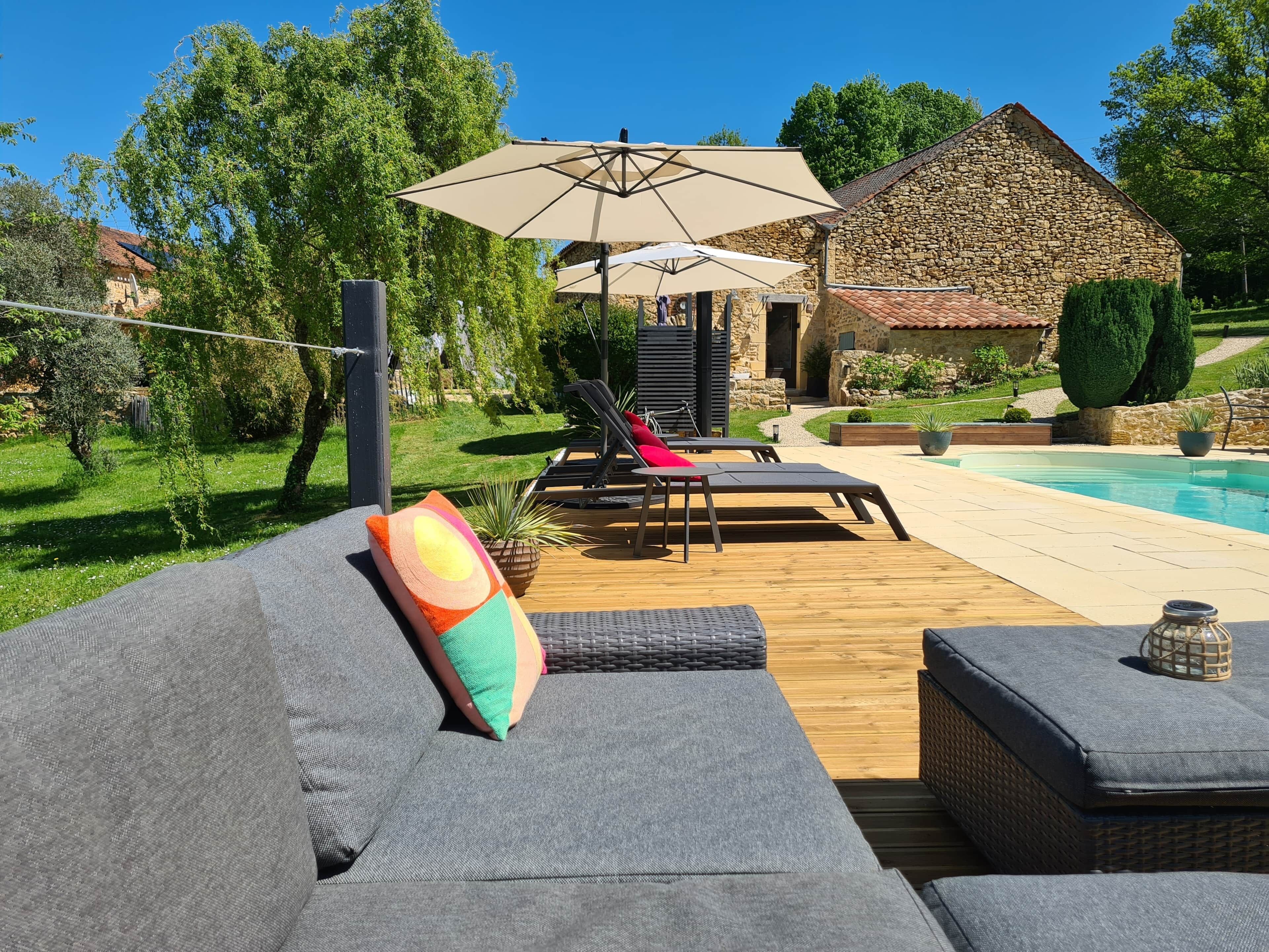 A poolside area with lounge chairs, a stone building, and a well-maintained garden.