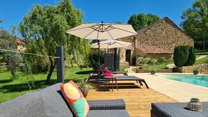 Zona junto a la piscina con sillones de descanso, un edificio de piedra y un jardín bien cuidado.
