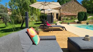 A poolside area with lounge chairs, a stone building, and a well-maintained garden.