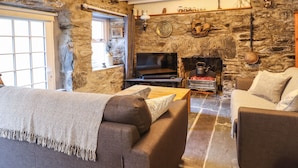 A cozy living room with stone walls, a fireplace, and a television. - Deu-ddrws (Barmouth)