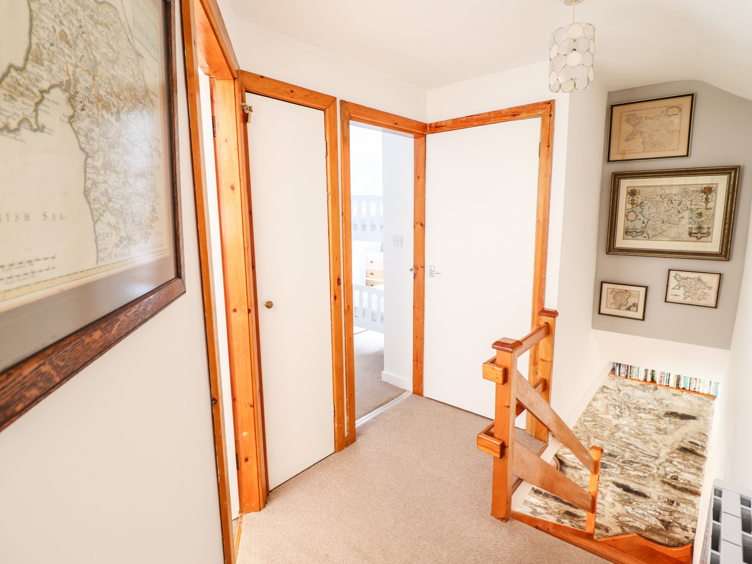 A hallway with wooden doors, a staircase, and a wall with framed maps.