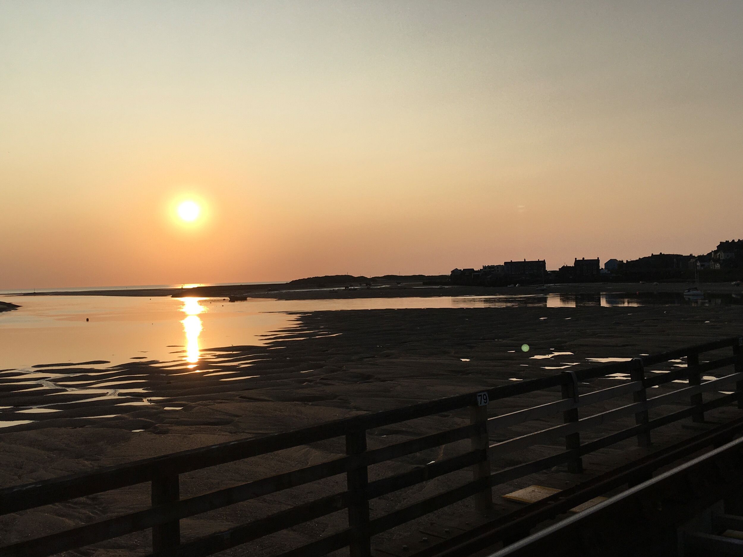 A sunset over a beach with a wooden walkway.