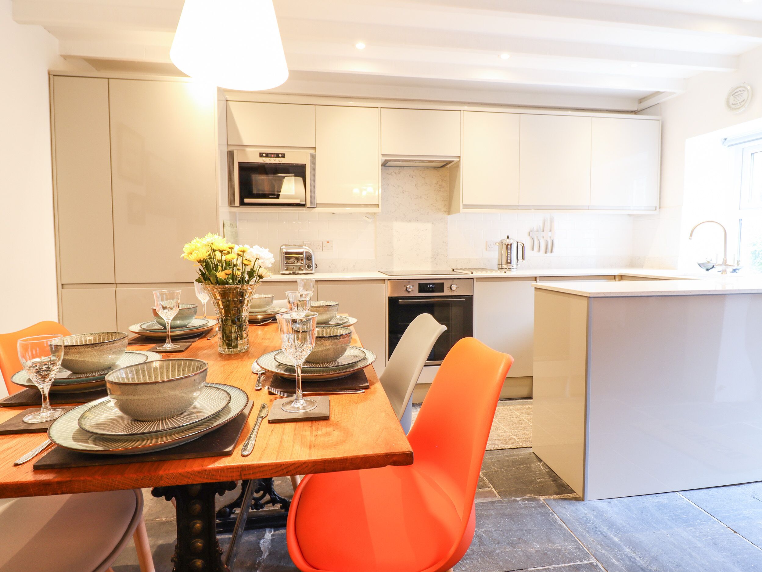 A modern kitchen with white cabinets, a built-in oven, and a dining area with a wooden table set for four.