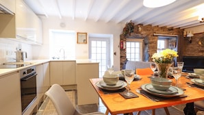 A modern kitchen with white cabinets, a built-in oven, and a dining area with a wooden table set for four. - Deu-ddrws (Barmouth)