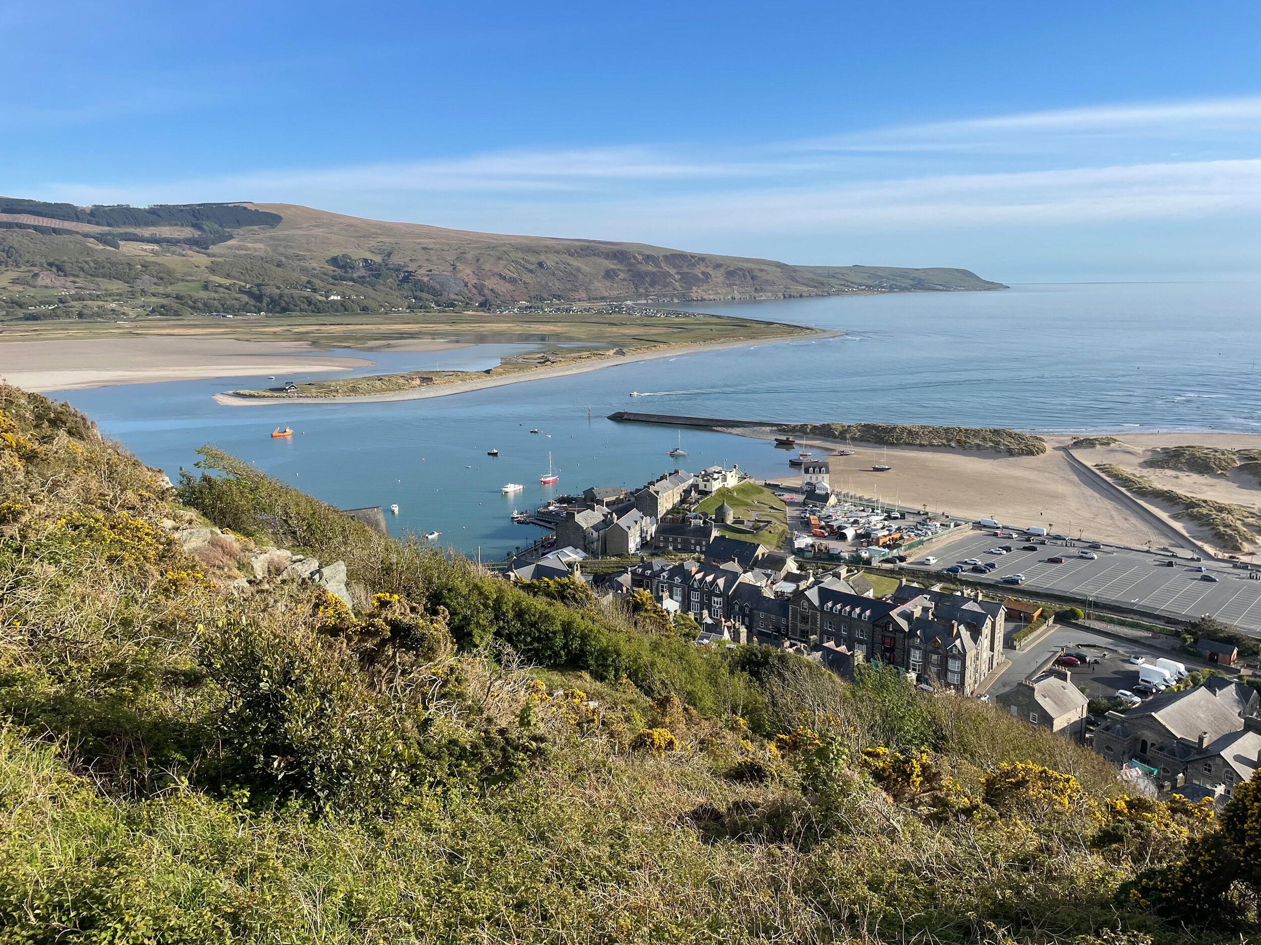A coastal town with a marina, sandy beach, and hilly landscape.