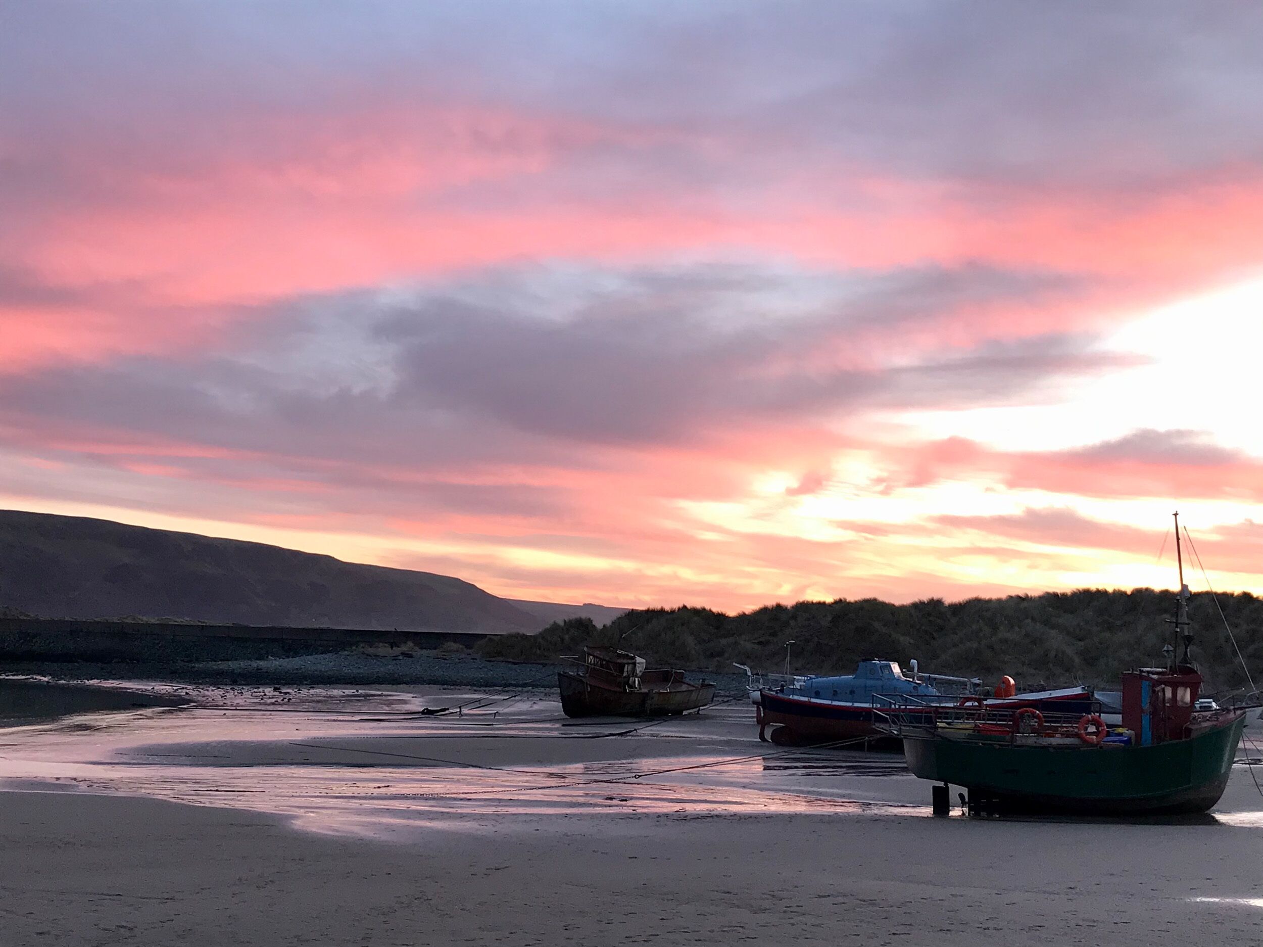 Boote liegen vor Anker an einem Strand, im Hintergrund ein Sonnenuntergang.