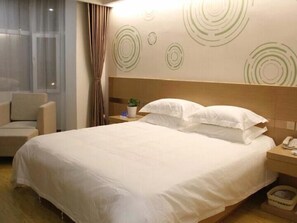 Una habitación de hotel con una cama grande, una mesita de noche con un teléfono, una planta pequeña y una silla.