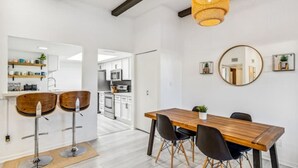 A modern kitchen with white cabinets, a central island, and a dining area with a wooden table and black chairs. - Desert Gem-Walk To Spring Training,ASU,Tempe Lake! (Tempe)