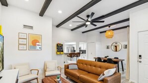 A modern living room with a brown leather sofa, white armchairs, a wooden coffee table, and a ceiling fan. - Desert Gem-Walk To Spring Training,ASU,Tempe Lake! (Tempe)