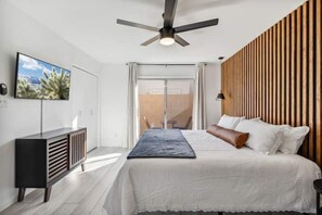 Een moderne slaapkamer met een bed, een aan de muur bevestigde televisie, een plafondventilator en een houten paneelwand.