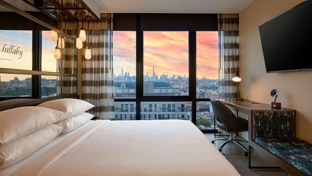 A hotel room with a large bed, a desk, a chair, and a TV. The room has a city view and a window with curtains. - Renaissance New York Harlem Hotel (New York)