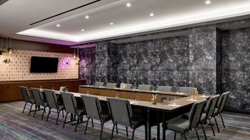 A conference room with a long table, multiple chairs, a flat-screen TV, and a patterned carpet.