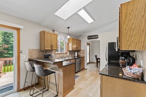 Une cuisine moderne avec des meubles en bois, un îlot central, des tabourets de bar et une vue sur l’extérieur.