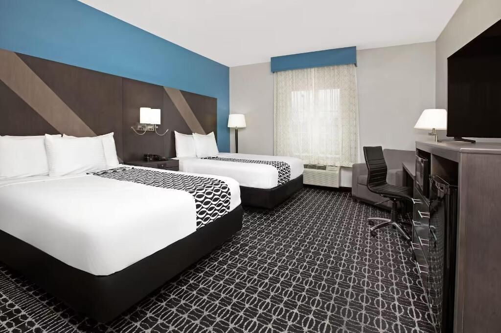 Habitación de hotel con dos camas, un escritorio, una silla, un televisor y una ventana con cortinas.