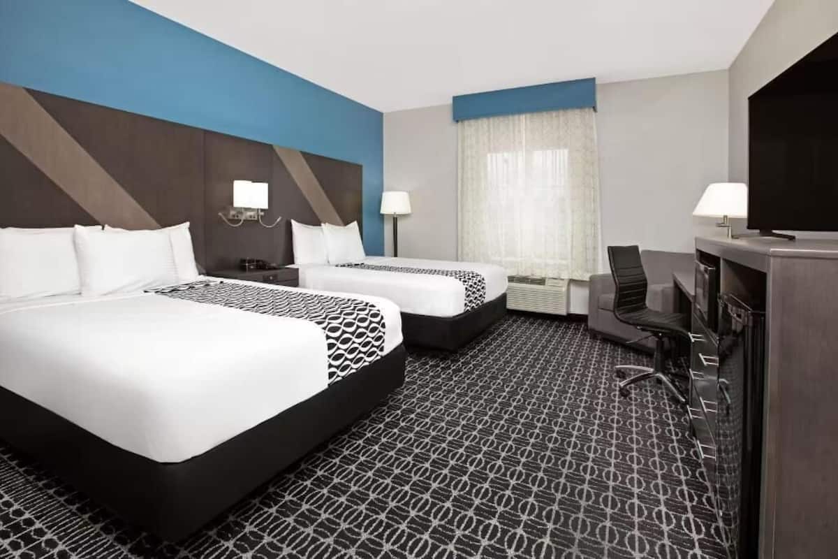 A hotel room with two beds, a desk, a chair, a TV, and a window with curtains.