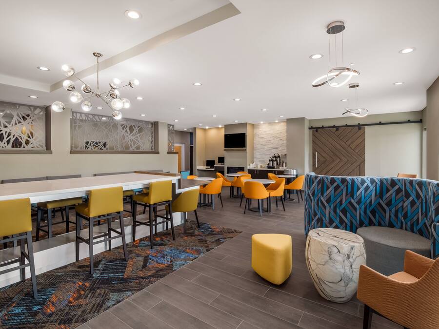 A modern dining area with a long table, yellow chairs, and a patterned rug.