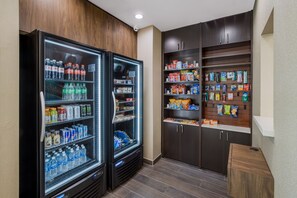 A refrigerated beverage cooler stocked with various drinks and a pantry with snacks and packaged goods. - La Quinta Inn & Suites by Wyndham Sulphur (Lake Charles) (Sulphur)