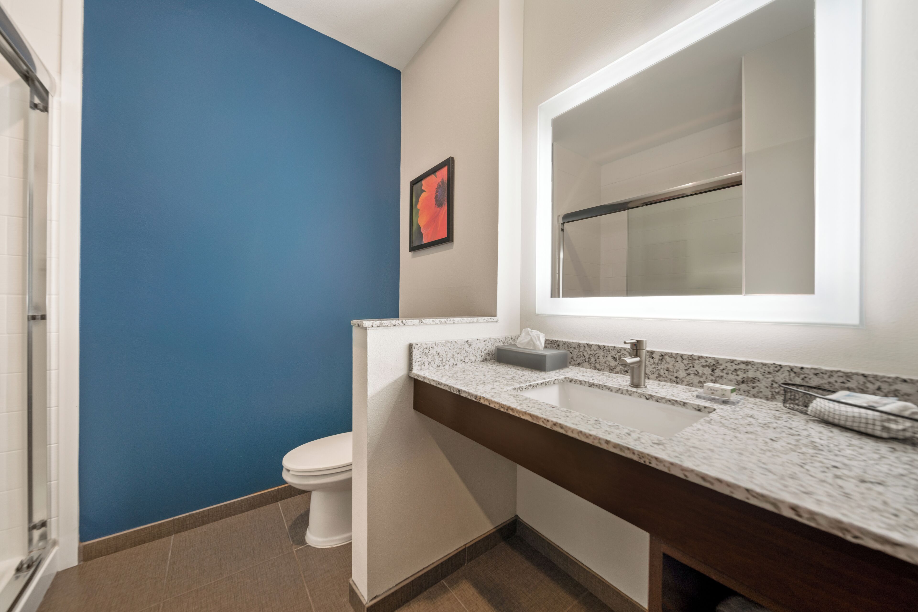 Une salle de bain avec un mur bleu, des toilettes blanches et un comptoir en granit surmonté d’un miroir.