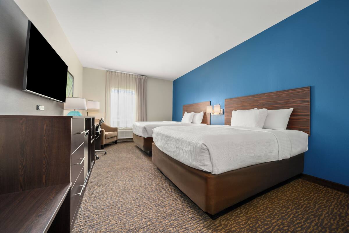A hotel room with a large bed, a desk, a TV, and a window with curtains.
