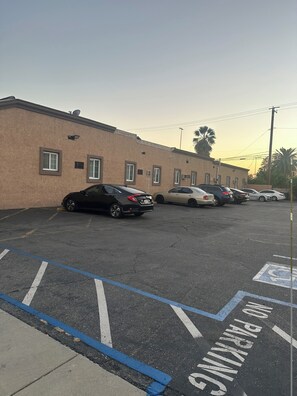 A parking lot with multiple cars parked in front of a building with a beige facade. - El Patio Hotel (San Bernardino)