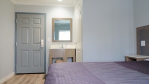 A bedroom with a bed, a wooden door, a bathroom with a sink, and a mirror.