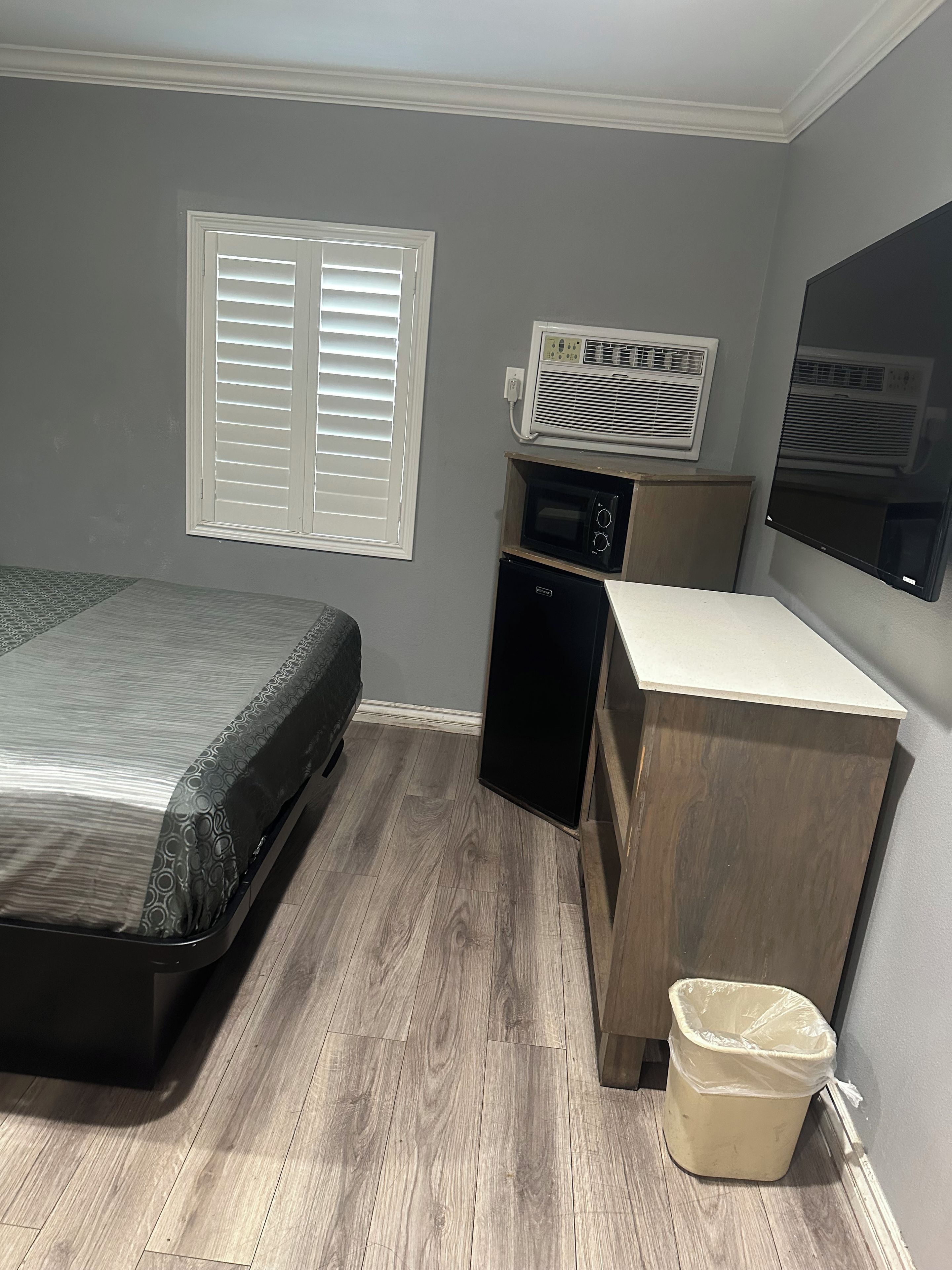 A bedroom with a bed, a small desk, a trash can, a heater, and a window with blinds.