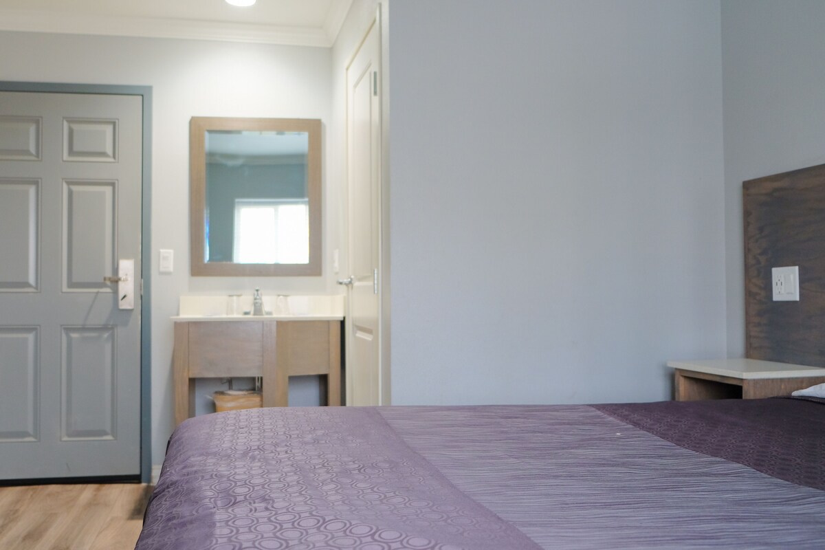 Una camera da letto con un letto, una porta in legno, un bagno con uno specchio e un comodino.