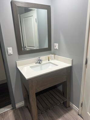 A bathroom with a white sink, wooden vanity, and a large mirror. - El Patio Hotel (San Bernardino)