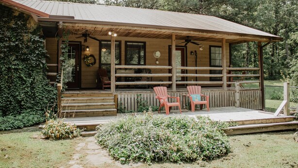 Une cabane en bois avec une véranda, deux chaises et un petit jardin.