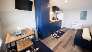 A compact kitchen with blue cabinets, a wooden dining table, a small trash bin, and a dark blue rug with a fish pattern. - Luxury Waterfront Tiny House (Harpswell)