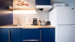 A modern kitchen with blue cabinets, a stainless steel sink, a coffee maker, and a microwave. - Luxury Waterfront Tiny House (Harpswell)