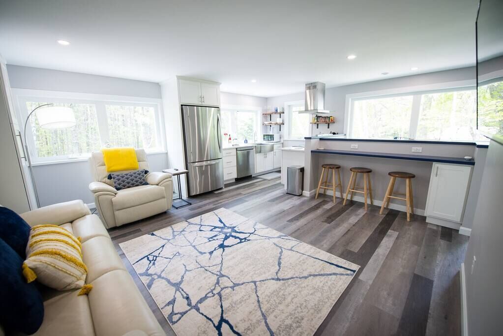Eine moderne Küche mit Edelstahlgeräten, ein Essbereich mit Hockern und ein Wohnzimmer mit Sofa und Teppich.