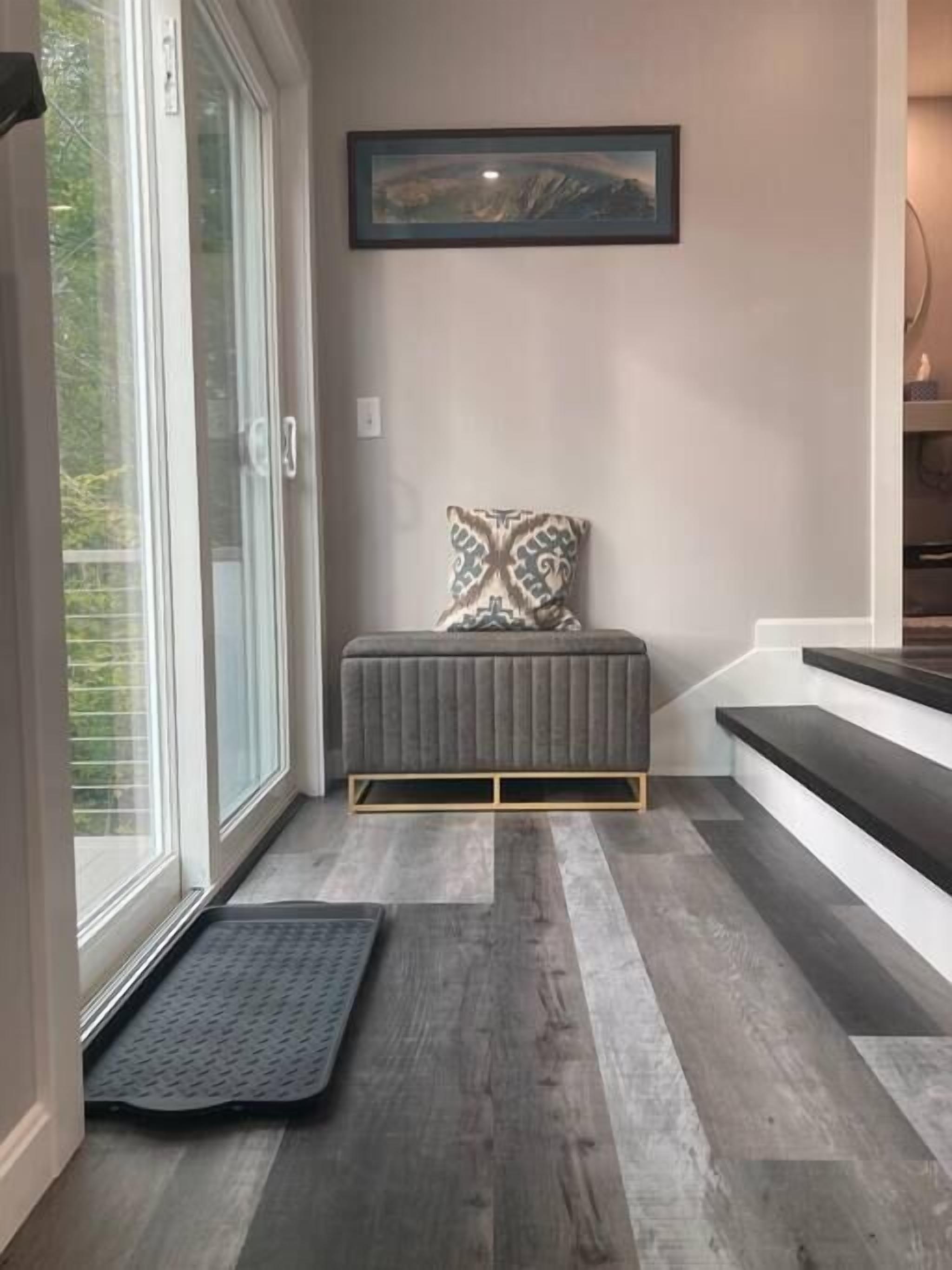 A modern entryway with a bench, a mat, and a framed artwork on the wall.