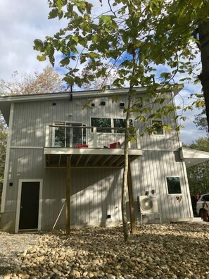 A two-story building with a balcony, a door, and an air conditioning unit. - Stylish Treetop Loft with Balcony and Ocean Views (Harpswell)